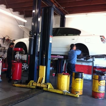 Two mechanics working on a white car raised on the two-post lift inside the Manila Brakes service bay