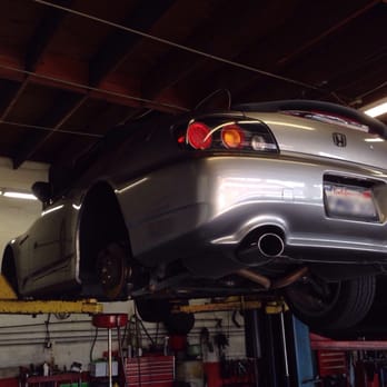 A silver Honda coupe raised on the lift, seen from behind, with tool chests along the shop wall